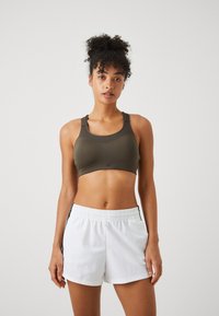 Sport-BH i olivengrønn, med en tettsittende design og brede stropper. Kombinert med hvite shorts, elastisk midje og svarte detaljer på siden.
