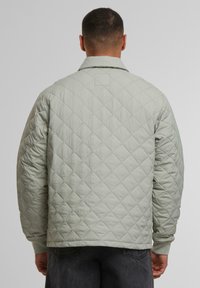 Hellgrüne gesteppte Jacke mit lässiger Passform, langen Ärmeln und Kragen. Strukturierter Rautenmuster über die gesamte Jacke. Normale Länge des Saums.