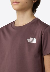 Bordová bavlněná trička s kulatým výstřihem a krátkými rukávy. Zajímavé bílé logo na levé části hrudi. Hladká textura.