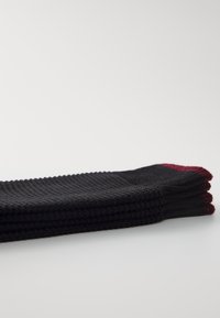 Calcetines negros de punto, enrollados de manera ordenada, con un patrón texturizado y acentos rojos en la parte superior. La tela parece suave y flexible.