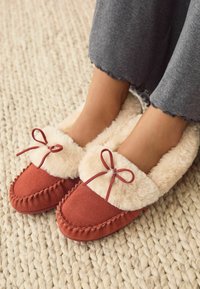 Røde ruskinds slippers med en fluffy cremeforing og matchende sløjfer. Har syede detaljer og en blød tekstur.
