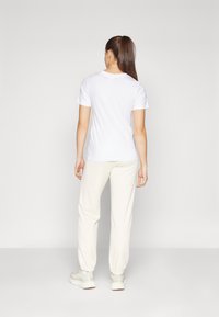 T-shirt blanc à manches courtes et pantalon de survêtement couleur crème, avec des poignets élastiques et une coupe décontractée, associés à des baskets de couleur claire.