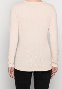 Maglione a maniche lunghe di un delicato colore rosa pallido, caratterizzato da un motivo a maglia testurizzata e traspirante. Presenta un collo tondo e polsini, orlo e dettagli laterali a costine.