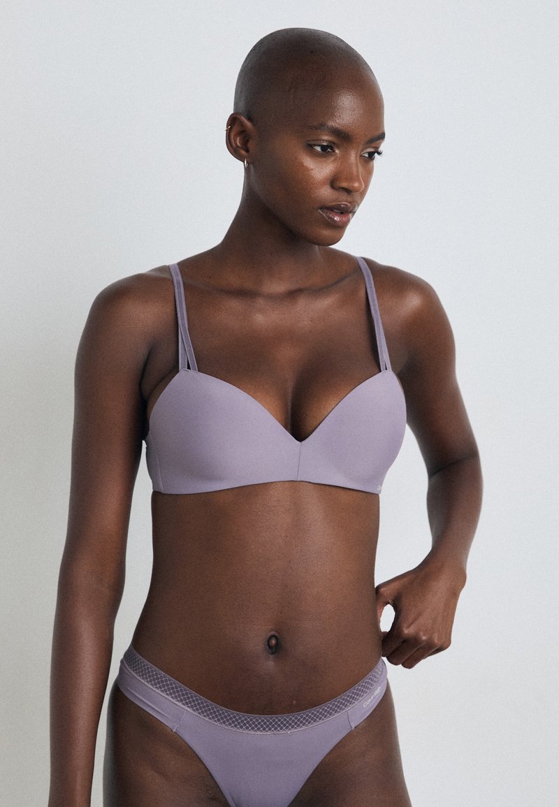 Lilac polstret bh med dyp utringning, justerbare tynne stropper, og matchende lilac truse med teksturert midjebånd. Glatt stofffinish.