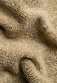 Beiger Frottee-Stoff, strukturiert mit einer weichen und flauschigen Oberfläche, in einer wellenförmigen Anordnung präsentiert, die das Material und die Farbe betont.