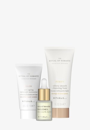 Drie huidverzorgingsproducten: een witte tube met het label "Glow" voor anti-verouderingshydraterende crème, een witte tube voor "Purify" reinigingsschuim, en een druppelflesje met "natural booster Bakuchiol."