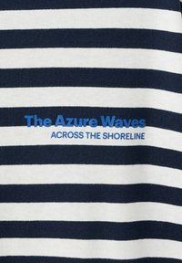 Tkanina s horizontalnimi modro-belimi črtami z modrim napisom »The Azure Waves« in »Across the Shoreline«.