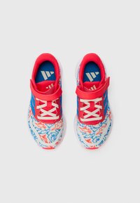 Baskets pour enfants avec un motif blanc, bleu et rouge, des sangles rouges, des lacets blancs et des semelles intérieures bleues arborant un logo blanc.