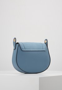 Borsa a tracolla in pelle blu con patta in camoscio e bordatura nera, caratterizzata da due dettagli in metallo color oro e una forma arrotondata.