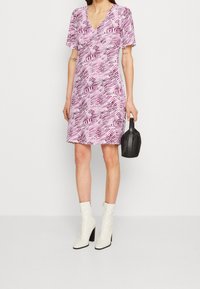 Kortärmad klänning i rosa och vitt med abstrakta mönster, V-ringning och utställd kjol. Matchas med svart handväska och vita stövlar med klack.