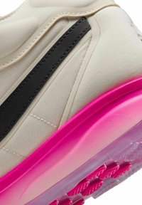 Gros plan sur une basket beige avec une bande noire et une semelle à dégradé rose vif, montrant les détails du tissu texturé et des coutures.