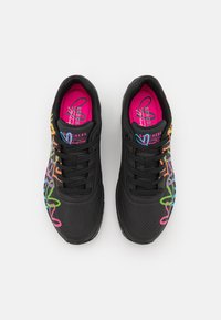 Schwarze Sportschuhe mit mehrfarbigen Zickzackmustern, durchlochter Textur, gepolsterten pinken Innensohlen und schwarzen Schnürsenkeln.