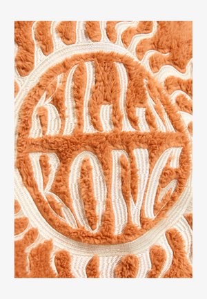 Oranje gestructureerde stof met pluchen borduursels van zonmotieven, voorzien van witte accentlijnen en gestileerde letters in een cirkelontwerp.