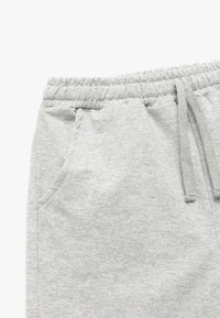Grå sweatpants med et struktureret stof, elastisk talje, snøre og sidelommer. Stoffet virker blødt og behageligt.