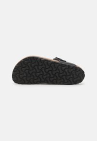 Black sandal with a textured rubber sole featuring a wavy pattern, cork midsole, and adjustable strap for fit. Sleek and minimal design.