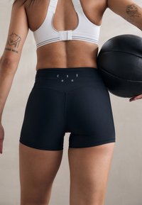 Black athletic shorts made of stretchy fabric, featuring a fitted design and a high waistband with printed letters near the back.