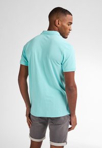 Polo shirt in cotone di un blu chiaro con colletto classico e maniche corte, abbinato a pantaloni corti grigi. Design semplice, senza motivi o loghi visibili.