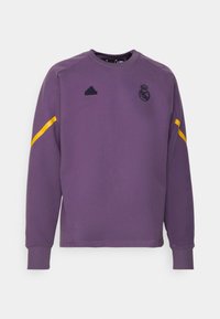 Sudadera morada con cuello redondo, mangas largas, raya amarilla en la manga y logotipo bordado en el pecho. Hecha de tela suave.