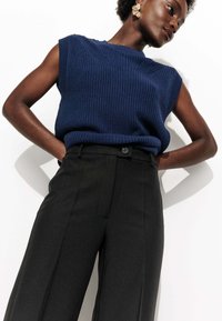 Débardeur tricoté bleu marine sans manches avec texture côtelée, associé à un pantalon noir taille haute avec fermeture à bouton et poches latérales.