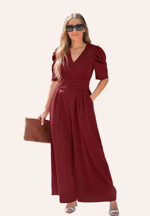 Combinaison bourgogne avec un décolleté en V, des manches bouffantes, un design plissé et des poches latérales. Associée à une pochette marron et des sandales argentées.