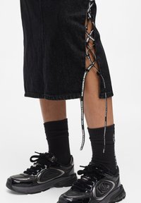 Svart denimkjol med snörning på sidorna som har en svart och vit märkesribbor. Kombinerad med svarta sneakers och ribbade svarta strumpor.