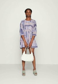 Vestido azul e branco com um padrão, de corte descontraído, mangas balão, sapatos de plataforma cinzentos e uma bolsa de palha branca.