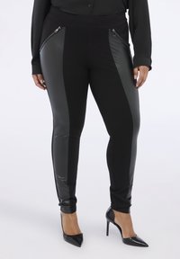 Svarta leggings med konstläderpaneler på sidan och zip-fickor, med en elastisk midja och en avsmalnande passform som sträcker sig ner till anklarna.