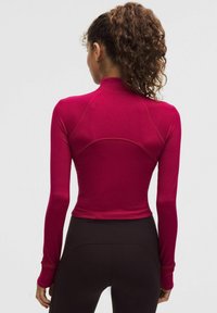 Ribota, pieguļoša, ar garām piedurknēm, blīvi fuksijas krāsā, ar augstu apkakli; izceļas ar precīzu šuvju izpildi un īsu dizainu.