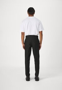 Pantalones negros con un corte entallado, que cuentan con bolsillos laterales y dos bolsillos traseros con botones, combinados con una camiseta blanca de corte holgado.