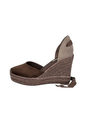 Zapato espadrille marrón con cuña, talón tejido, puntera cerrada y correa para atar en el tobillo sobre fondo blanco.