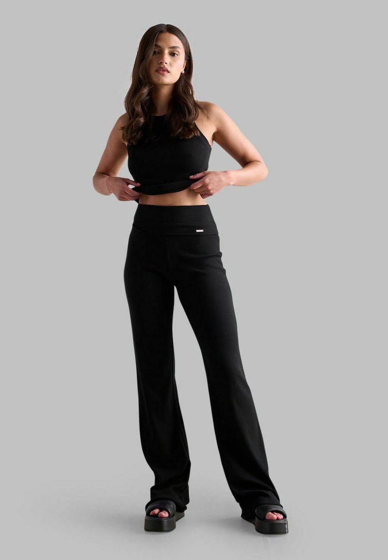 Schwarzes Cropped Top und hochgeschnittene schwarze Hose aus elastischem Material, mit glatter Textur und minimalistischer Gestaltung. Schwarze Plateausandalen.