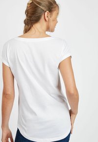 Valge T-särk pehmest puuvillamaterjalist, ümmarguse kaelusega ja lühikeste üleskeeratud varrukatega. Tagaküljel on kõveralt kujundatud ääreosa.