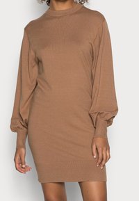 Robe longue en tricot marron à manches longues, avec un col montant, des manches bouffantes et des poignets et un ourlet côtelés. Texture douce, silhouette ajustée, longueur mi-cuisse.