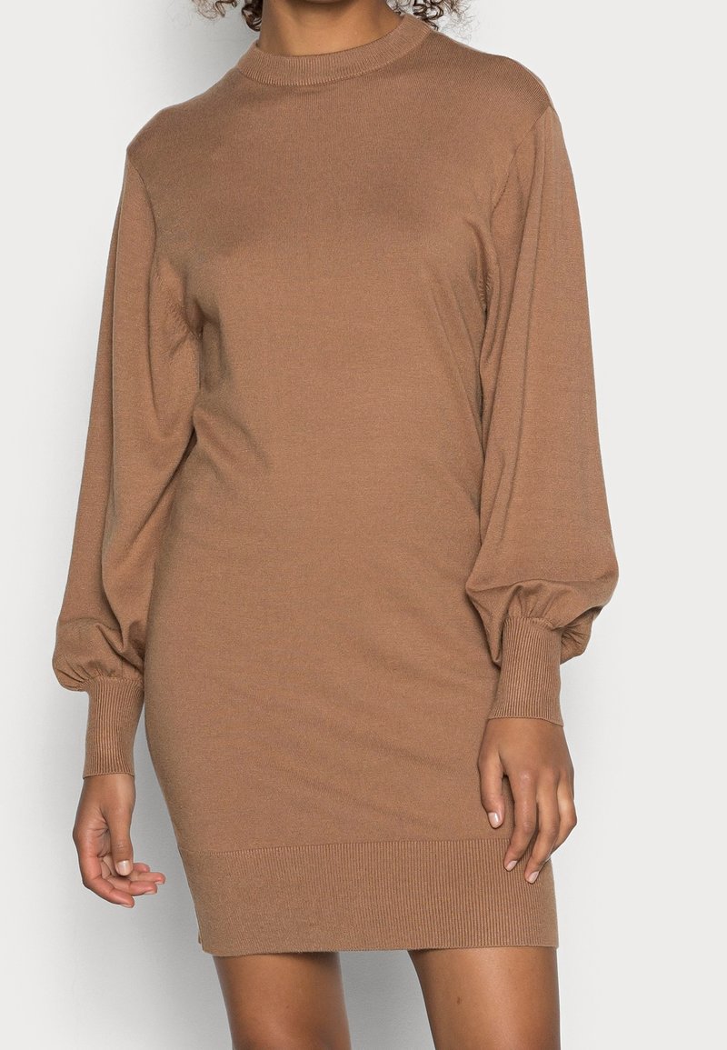 Robe longue en tricot marron à manches longues, avec un col montant, des manches bouffantes et des poignets et un ourlet côtelés. Texture douce, silhouette ajustée, longueur mi-cuisse.