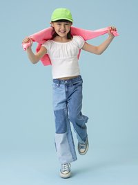 Svetlo modra kapa, bela majica s kratkimi rokavi, barvno blokirane jeans hlače in svetlo modri čevlji. Drži roza pulover čez ramena.