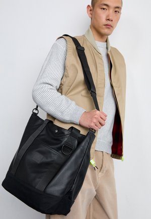 Fekete bőr bevásárlótáska szövet részletekkel, erős pánttal, nagy fő rekesszel és egy kisebb elülső zsebbel.