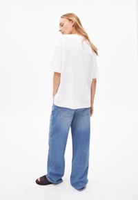 Lockere weiße Baumwoll-T-Shirts mit kurzen Ärmeln, kombiniert mit hellblauen, weiten Jeans. Die Jeans haben ein klassisches Fünf-Taschen-Design.