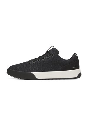 Baskets basses noires avec lacets noirs, semelle intermédiaire blanche, semelle extérieure noire et étiquette imperméable près du talon.