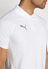 Weißes Poloshirt aus strukturiertem Stoff mit klassischem Kragen, zwei Knöpfen und einem grauen Puma-Logo auf der linken Brust.