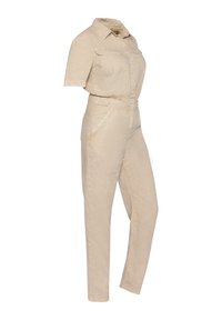 Tuta beige chiaro con maniche corte, due tasche frontali, chiusura con bottoni e gambe affusolate in tessuto testurizzato.
