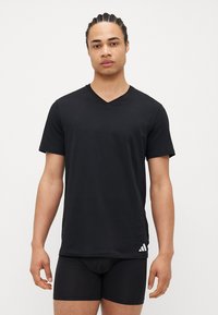 Μαύρο μπλουζάκι v-neck φτιαγμένο από μαλακό ύφασμα, με κοντά μανίκια και λευκό λογότυπο κοντά στο στρίφωμα. Φοριέται με μαύρα σλίπ.