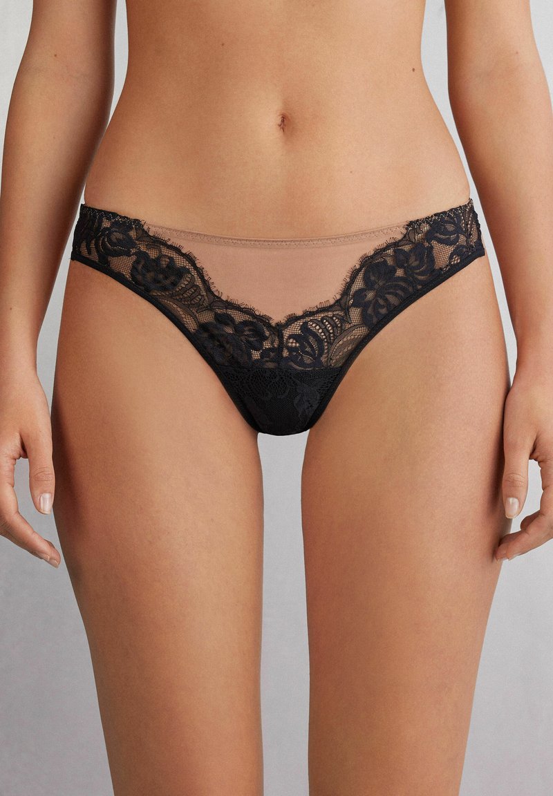 Zwarte kantstring met bloemenpatroon, doorschijnende nude stof aan de voorkant en een gladde tailleband. Het kant heeft verfijnde details en randen.