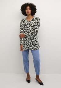 Tunic floreale in bianco e nero con maniche lunghe, scollo a V e vestibilità ampia, abbinata a jeans dritti blu chiaro e scarpe nere a punta.