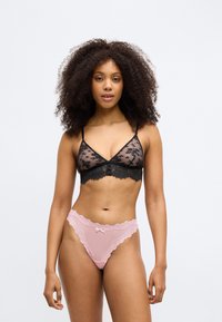 Bralette en dentelle noire avec des motifs floraux et des bords festonnés, associé à un string rose avec une bordure en dentelle et un détail en noeud.