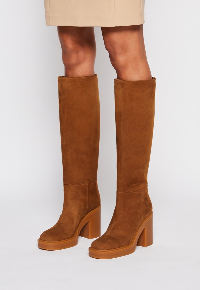 Bottes montantes en daim marron avec un talon bloc, présentant une texture lisse et un bout arrondi. Talon large et solide pour la stabilité.