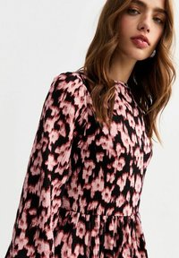 Vestido con estampado rosa y negro de mangas largas, que presenta una tela texturizada y una falda acampanada, mostrando un diseño de impresión floral.