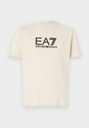 T-shirt in cotone crema con maniche corte, caratterizzata da un grande logo grafico nero "EA7 EMPORIO ARMANI" sul davanti.