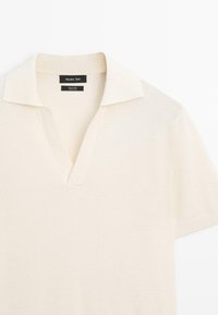 Licht beige poloshirt van 100% katoen, met een V-hals, korte mouwen en een gestructureerd breipatroon. Klassiek kraagontwerp.