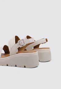 Sandalias de plataforma blancas con correas anchas, hebilla ajustable y suela texturizada. Presentan un acabado de cuero suave y una plantilla de madera natural.