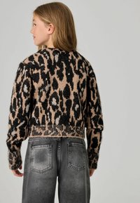 Gestreifter Leopardenmuster-Pullover in Beige und Schwarz, mit einem verkürzten Design und geripptem Saum. Kombiniert mit ausgebleichten grauen Jeans.